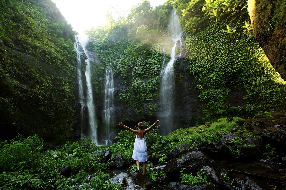 woman in white raising arms at Sekumpul Waterfall