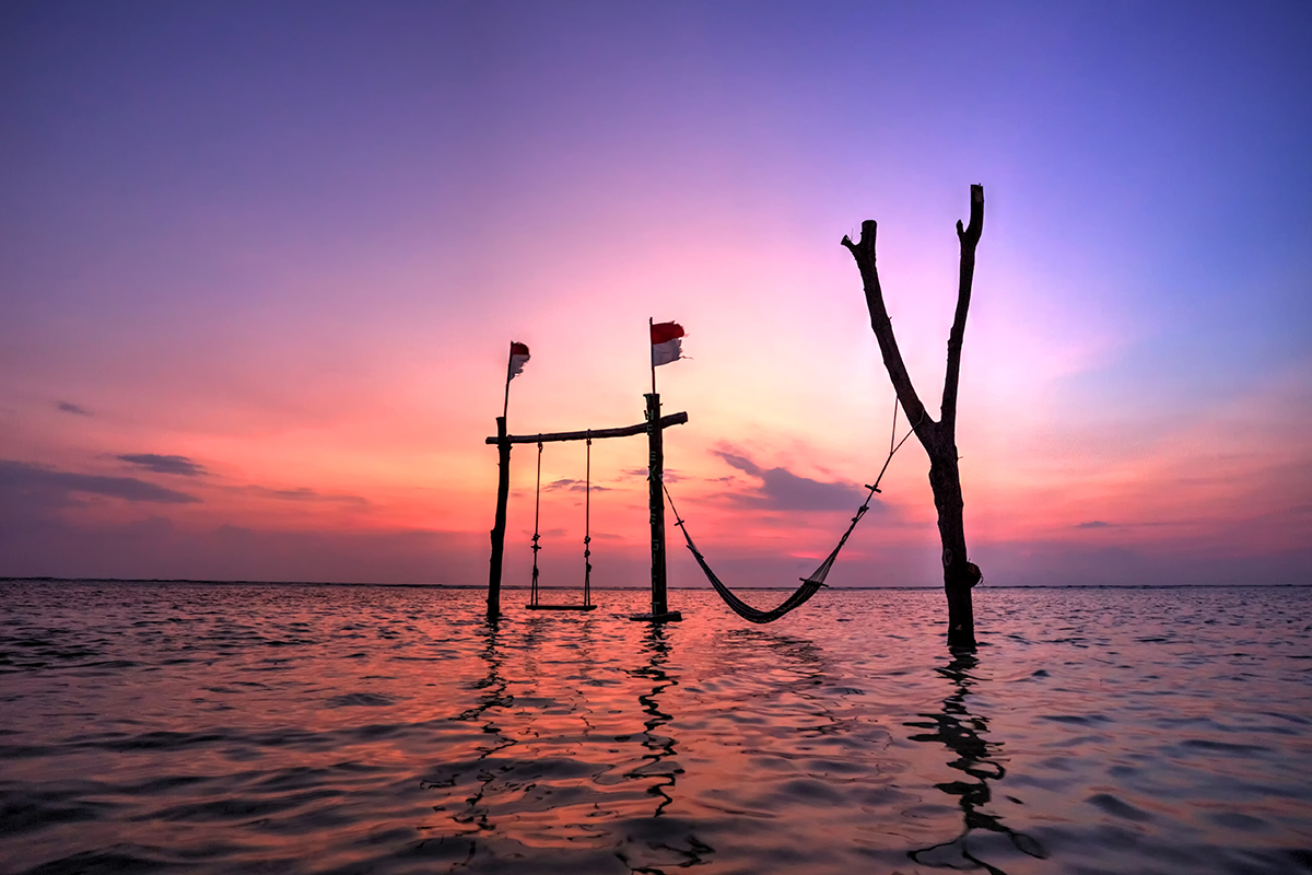 a wooden swing somewhere in Lombok, West Nusa Tenggara, opaque waters, sunset, two Indonesian flags